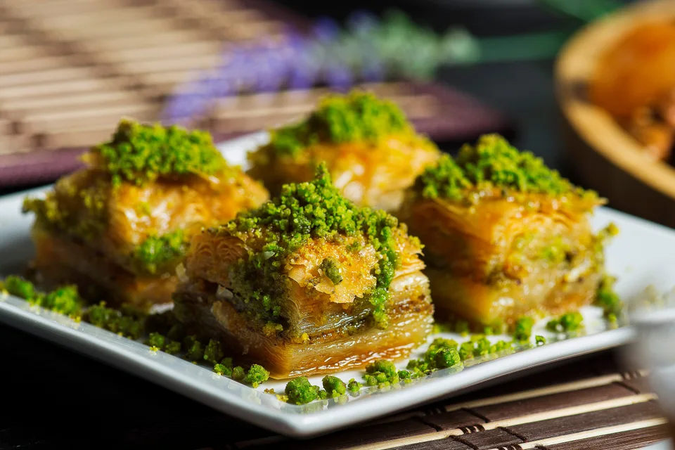 BookNoFees: Exempelbild: Fyra lager baklava toppade med krossade pistagenötter på en vit tallrik
