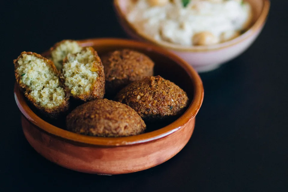 BookNoFees: Exempelbild: Falafelbollar, inklusive en uppskuren bit, i en skål med hummus bakom